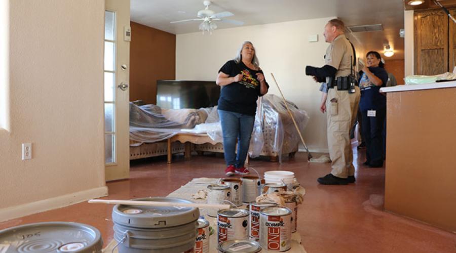 Paint supplies on a tarp inside of a home; people in the background