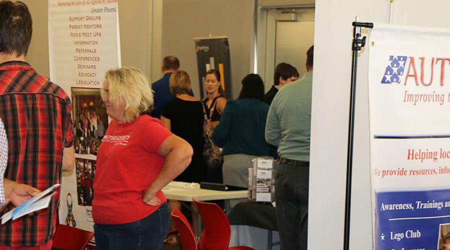 Men and women, employers standing behind tables, with the banner Autism Society in the background