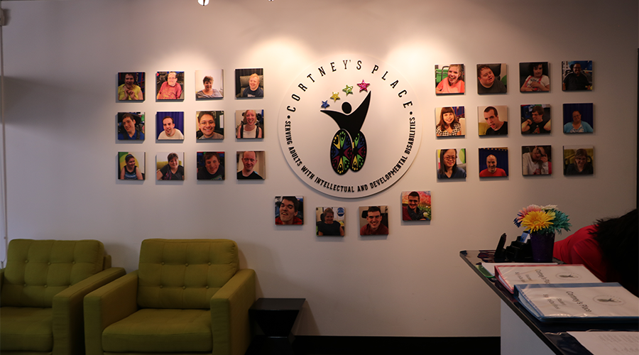 A lobby wall displays the Cortney’s Place logo, which is surrounded by head shots of various students.