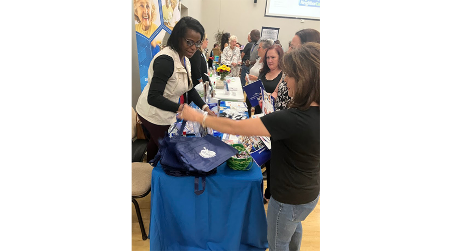 People at a table at an indoor event with pamphlets and tote bags.