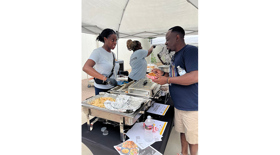 People at a food stall serving and receiving food under a canopy.
