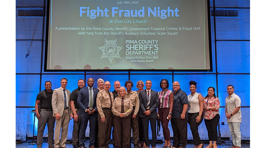 A group of sixteen people stands in front of a screen displaying "Fight Fraud Night" information.