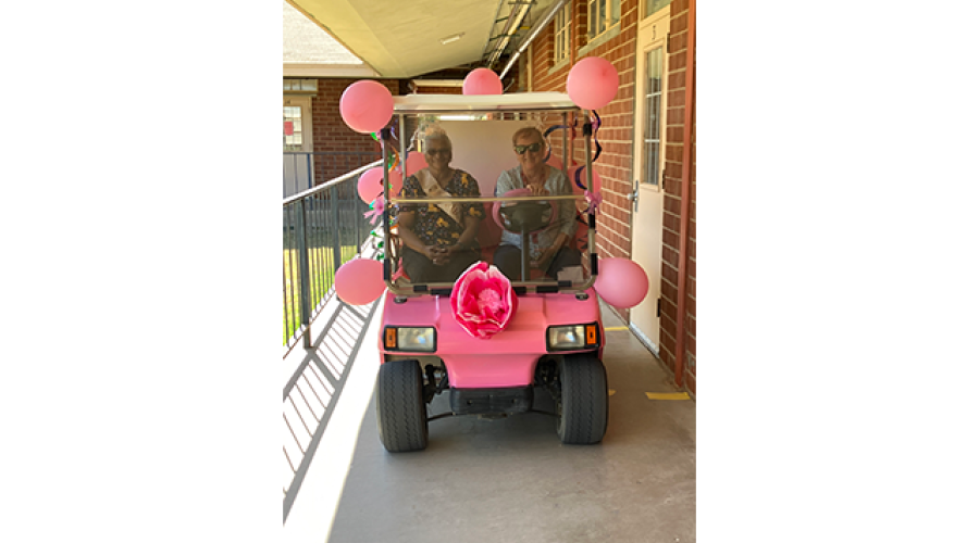 two women riding in a pink golfcart that is decorated with pink balloons