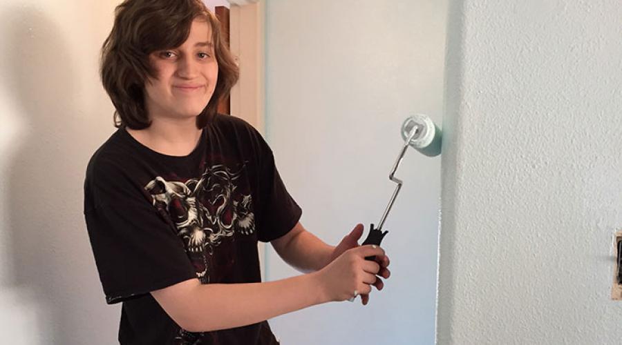 Teen boy uses a roller to paint wall inside of a home 