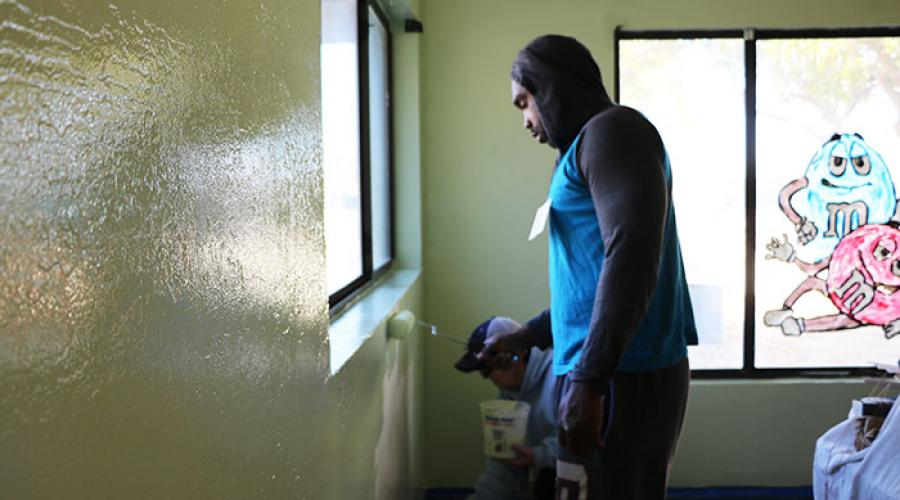 Two men paint wall near a window inside of a home