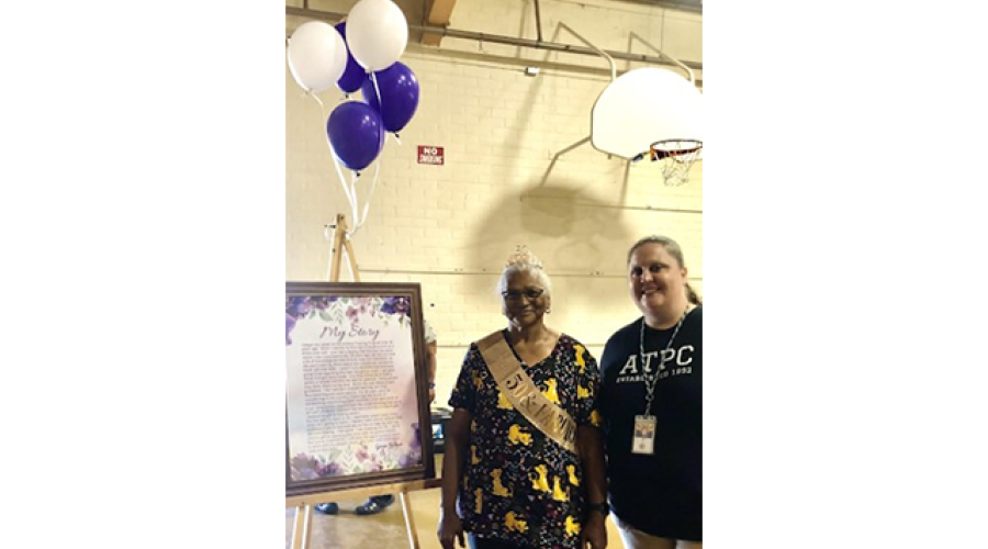 two women stand next to a balloon-decorated display that reads "My Story"