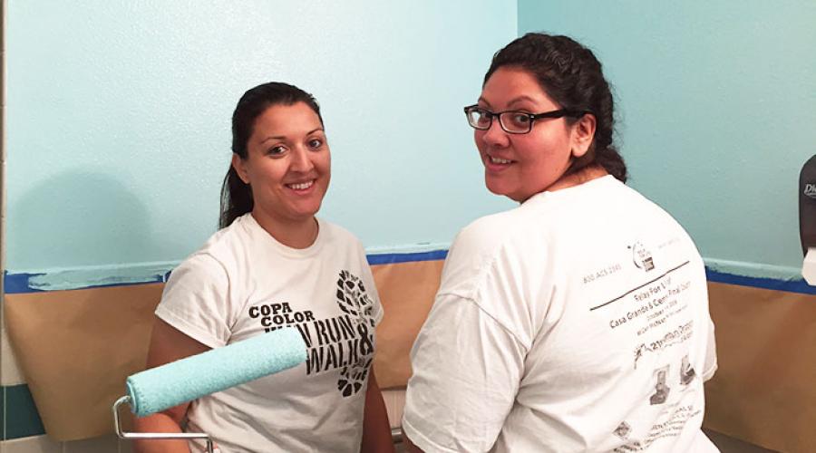 Two women pose for photos in front of partially painted wall