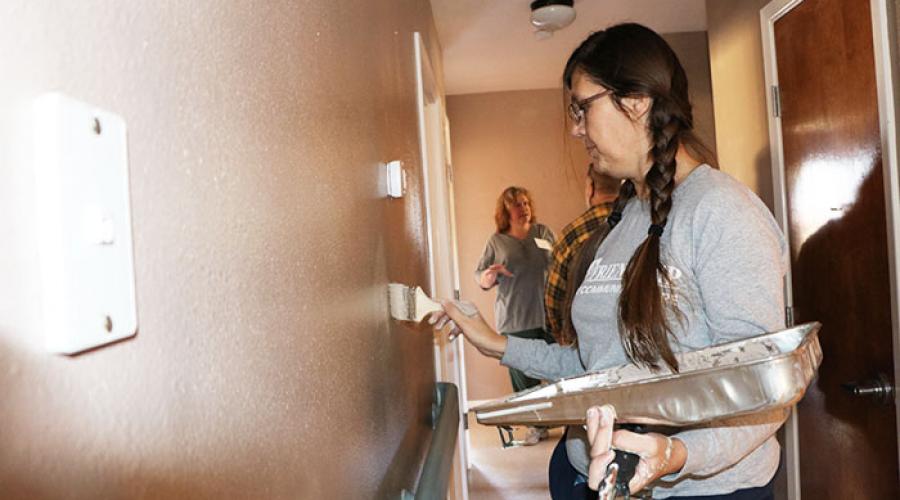 Woman paints wall inside of a home with a paint brush