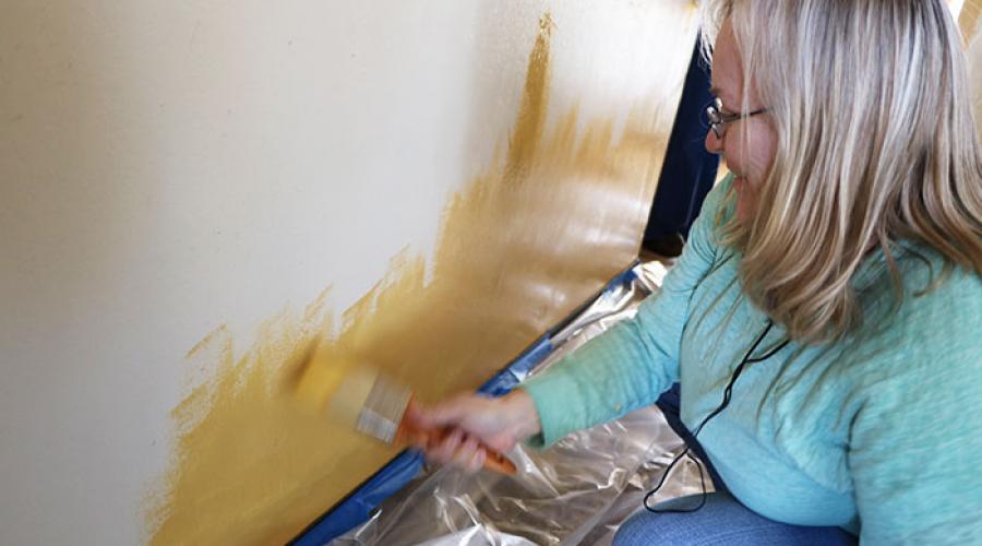 Woman using a paint brush to paint a lower wall in side of a home