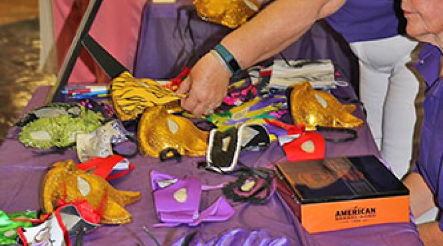 two women sort through a variety of masquerade masks that are displayed on a table