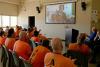a group of men wearing orange t-shirts watch a presentation on a screen