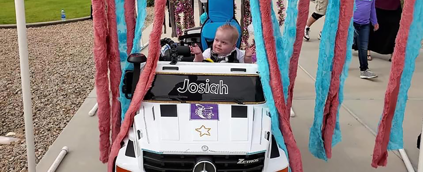 Toddler drives an adapted toy vehicle through a pretend car wash.