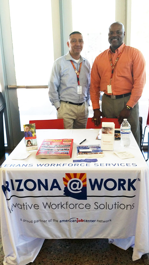 Two men stand behind a booth at a job fair