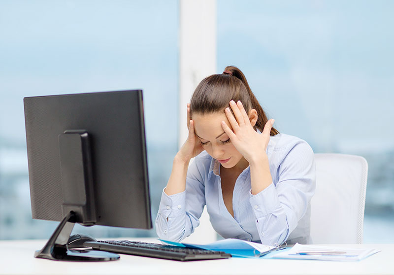 woman sits at desk holding her head in her hands