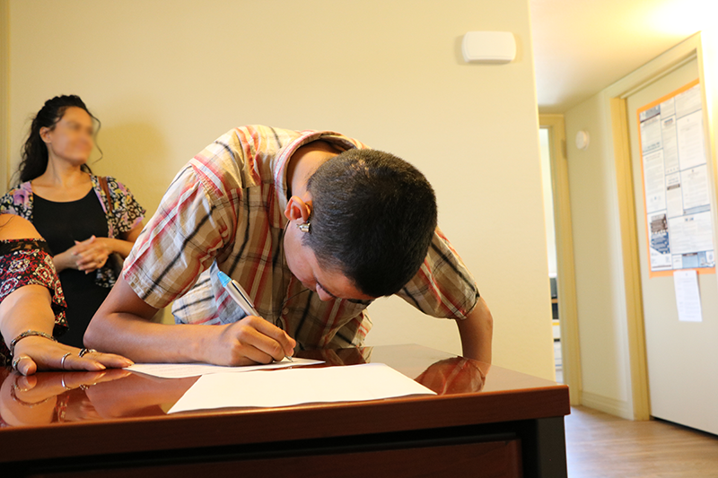 a young man signs a document on a table top