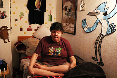 a 30-year-old man sits cross-legged on his bed
