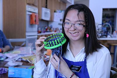 Young Asian-American woman holds up the loom she uses to knit baby hats.